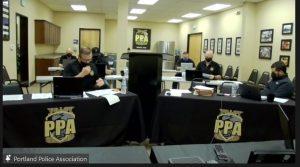 Screenshot from PPA contract negotions Zoom call. PPA officials sit at tables at computers, the front two tables are draped with a black tablecloth, with the PPA logo. The wall has a framed thin blue line flag, and the six people in the room all look like the same middle-aged white guy. The man at the front table is not wearing his mask properly, leaving his nose exposed.